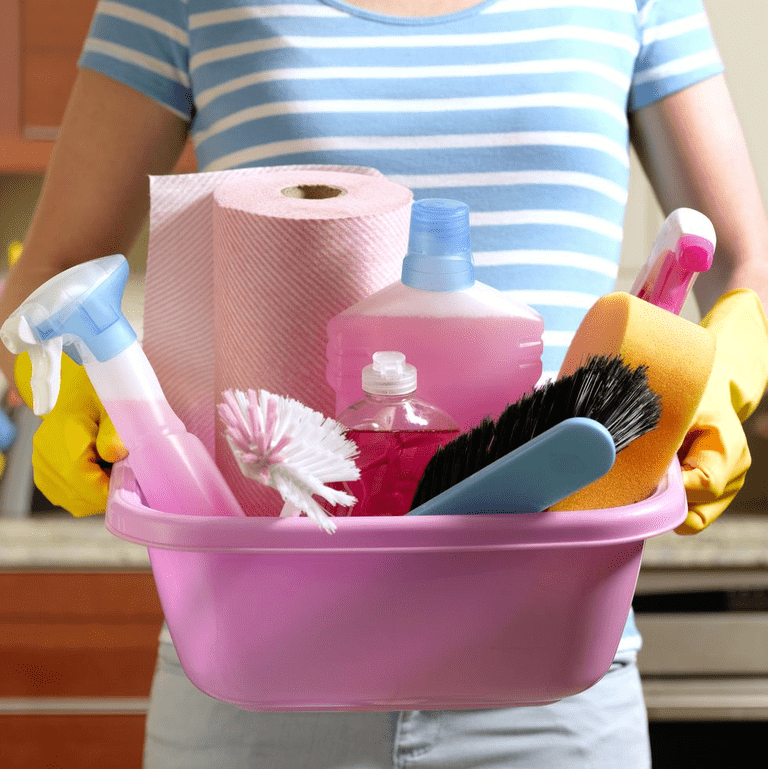A woman holding a pink basket full of cleaning supplies.